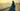 Woman in a deep teal embroidered abaya along the Bahrain Corniche at sunset